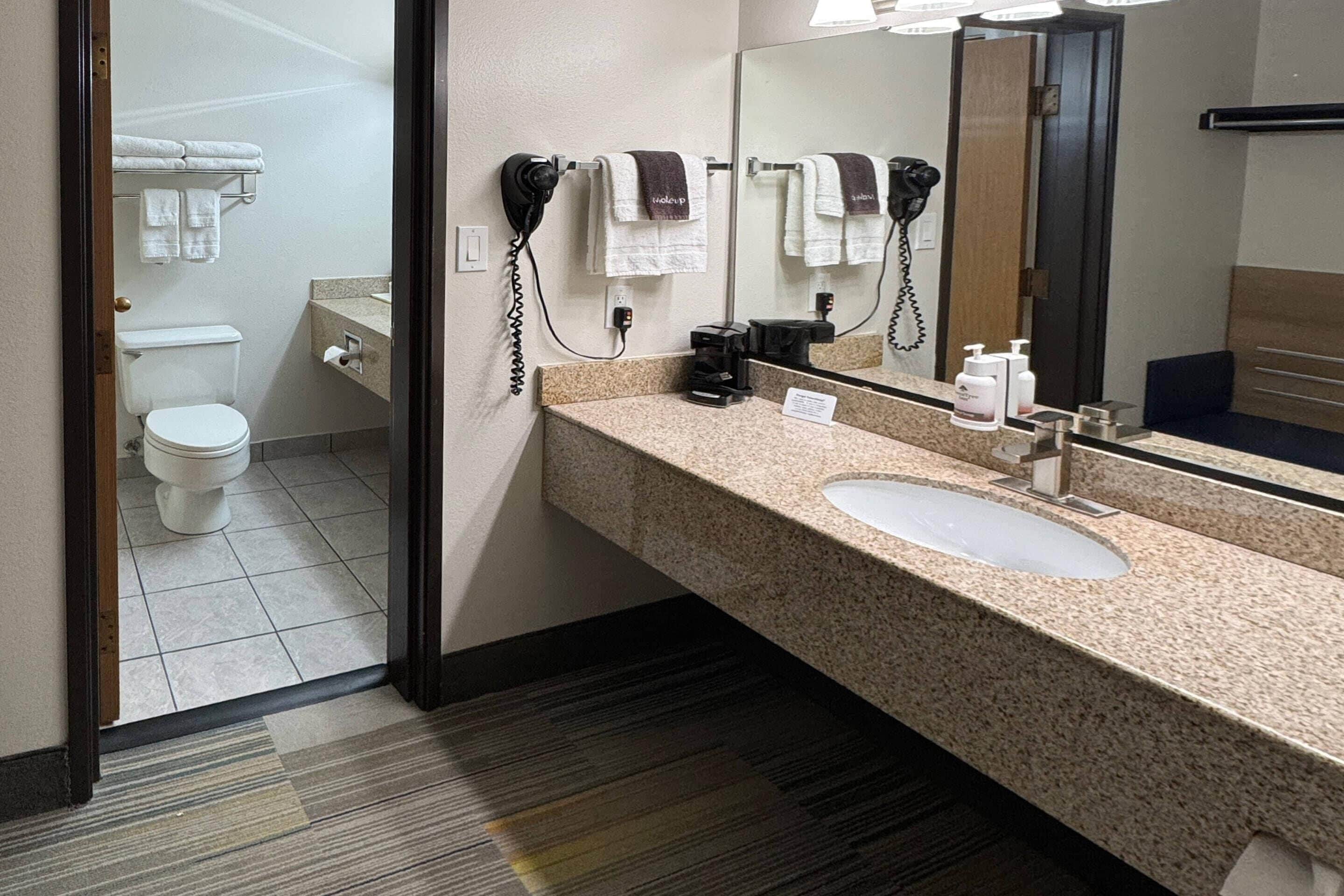 A hotel bathroom with a sink, mirror, towel rack, and hair dryer.