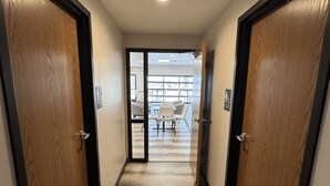 A hallway with wooden doors and a carpeted floor leading to a seating area with tables and chairs.