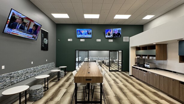 A modern conference room with a long table, multiple screens, and a kitchenette.