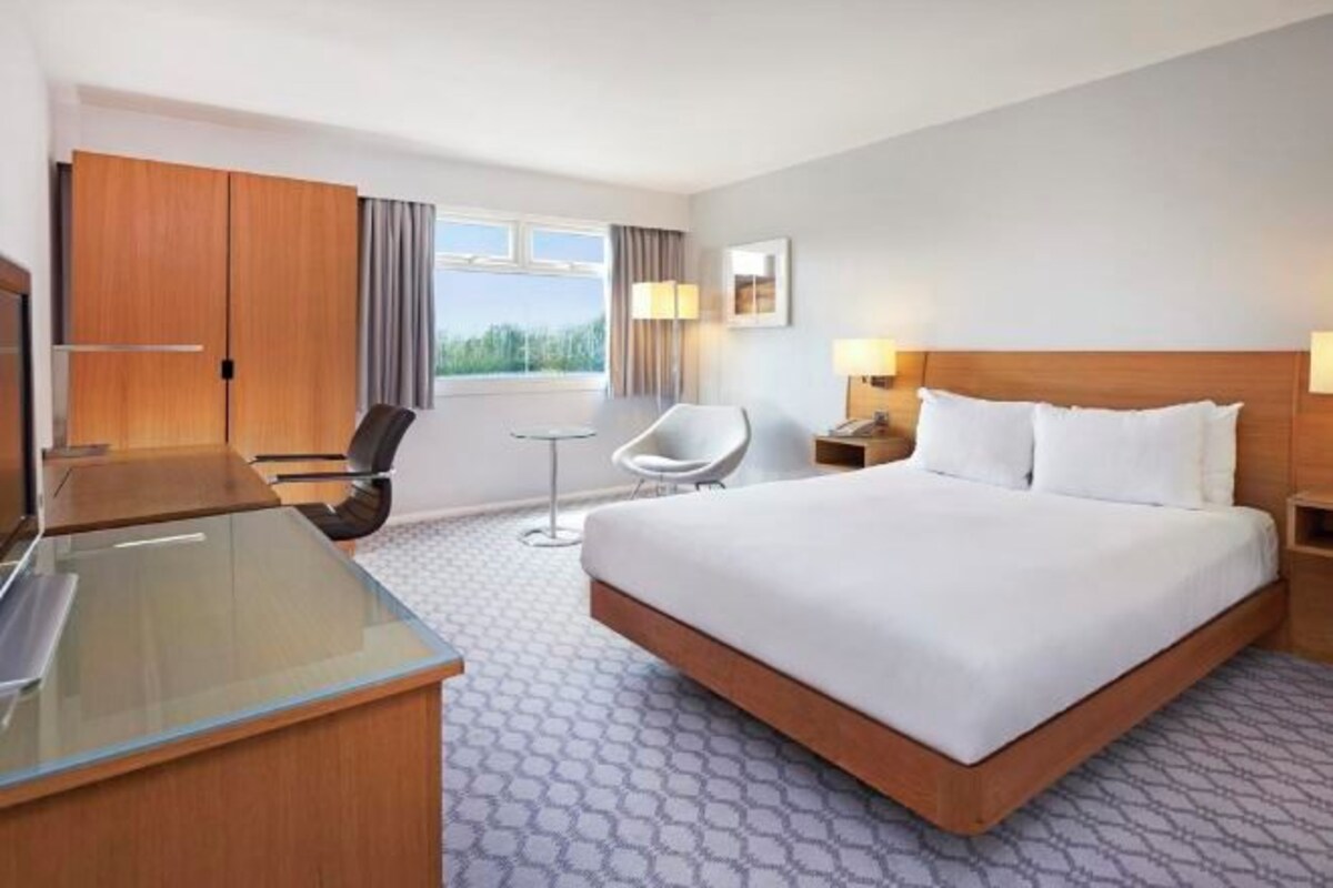 A hotel room with a large bed, a desk, a chair, and a small table.