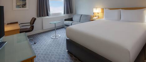 Habitación de hotel con cama, escritorio, silla, mesita y ventana con cortinas.