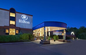 Un hotel amb un cartell ben visible de Hilton, entrada coberta i façana de maó.