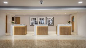 Eine Hotelrezeption mit drei Holztresen, einem Marmorboden und drei gerahmten Blumenbildern an der Wand.