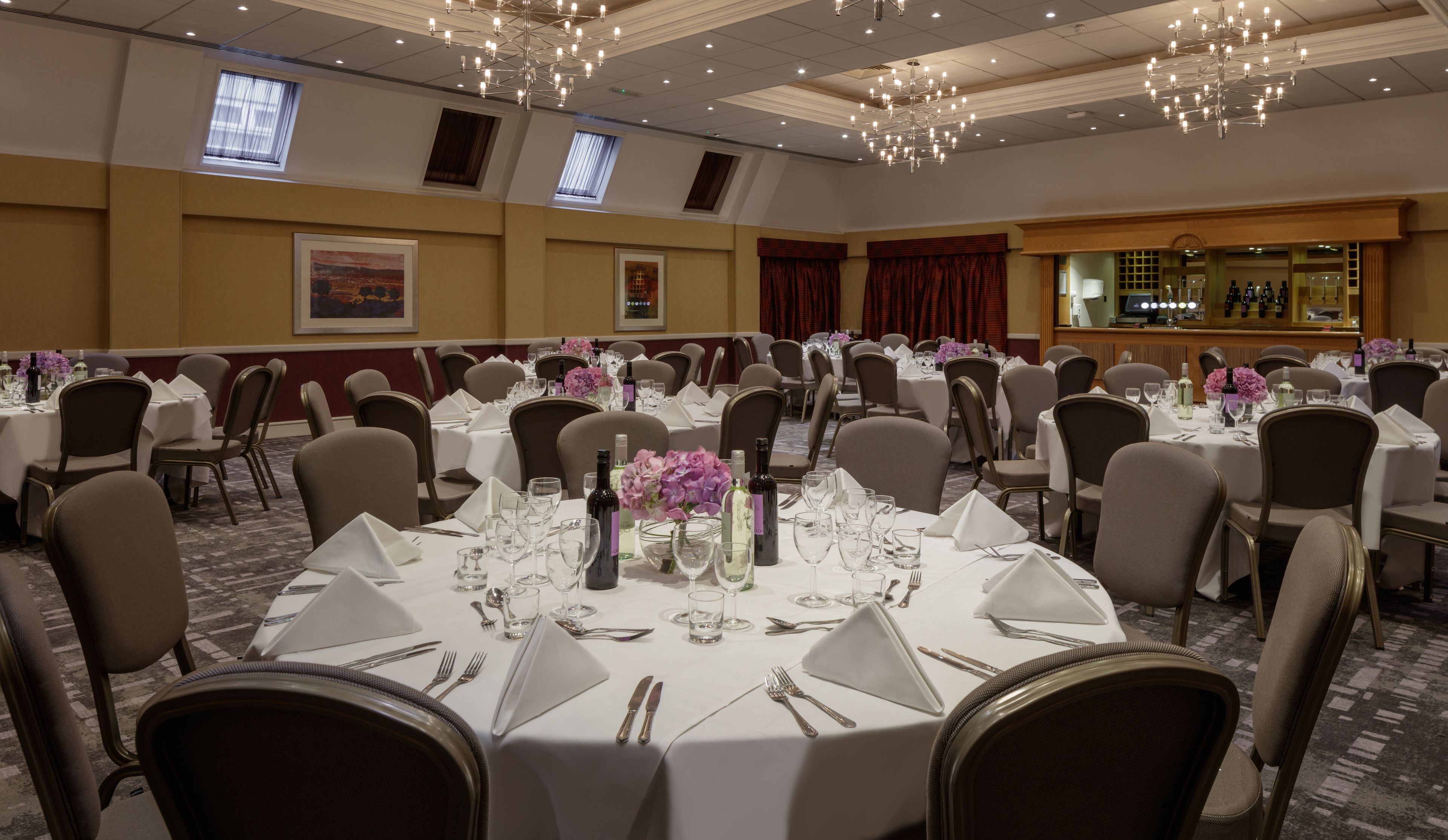 Un salón de banquetes con mesas redondas dispuestas para comer, con manteles blancos y cubertería.