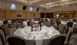 Une salle de banquet avec des tables rondes dressées pour le repas, ornées de nappes blanches et de couverts en argent.