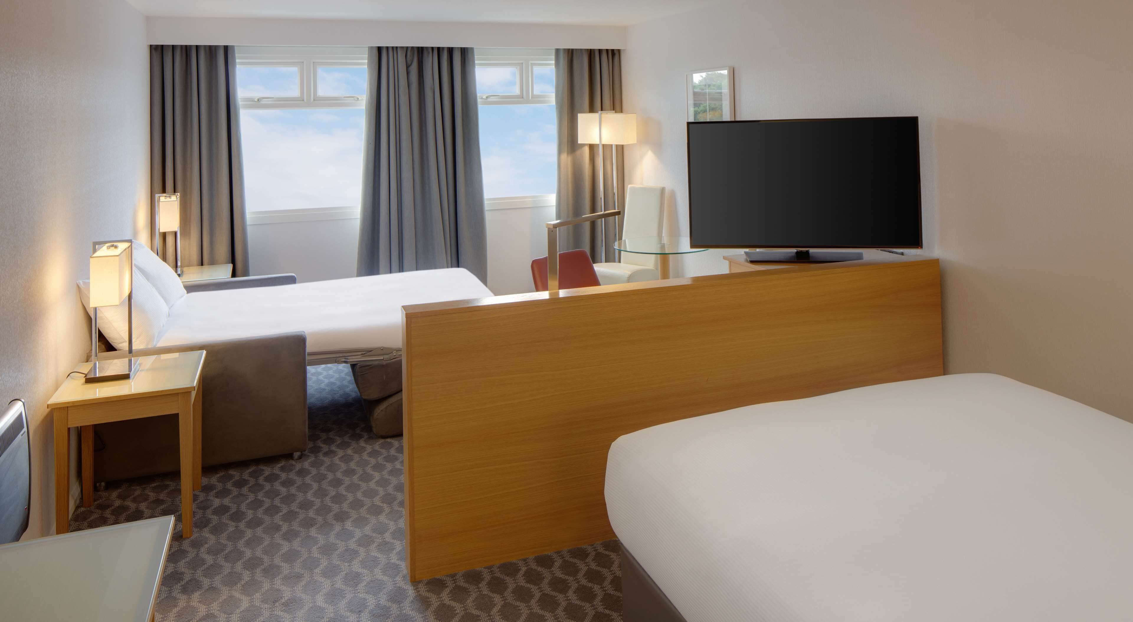 Ein Hotelzimmer mit Bett, Schreibtisch, Stuhl, Fernseher und einem Fenster mit Vorhängen.