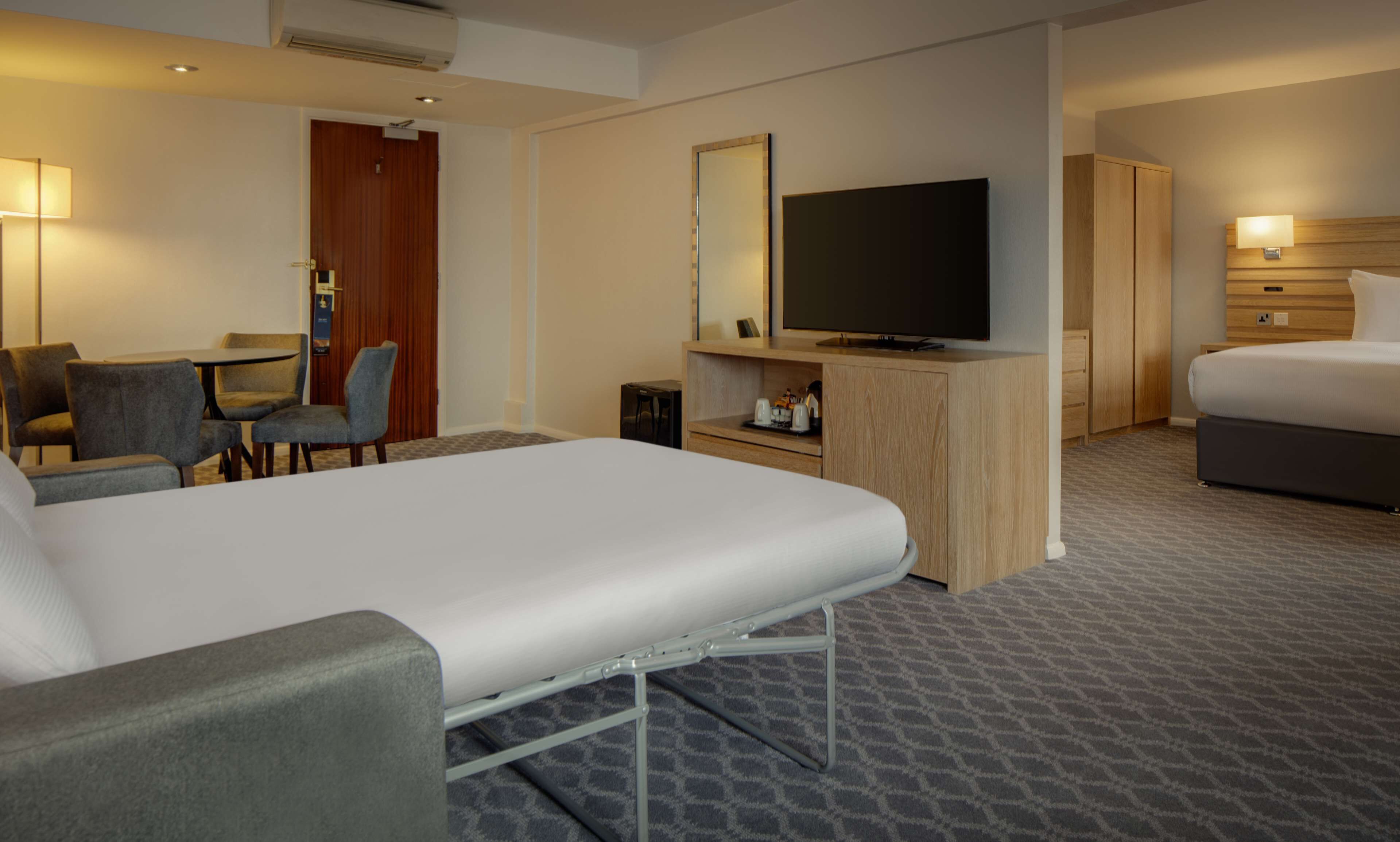 A hotel room with a bed, a desk, a television, and a seating area with chairs.