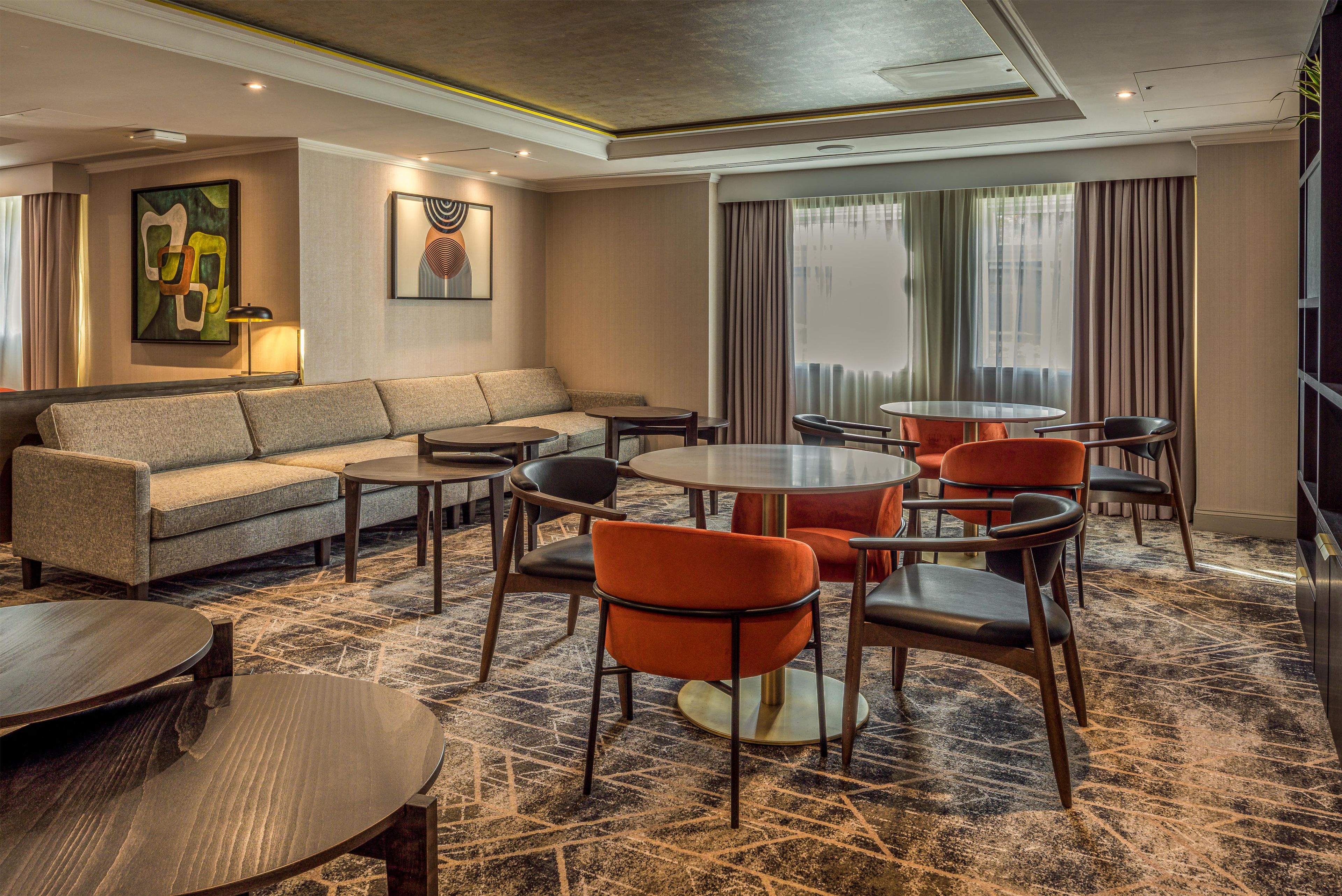 A hotel lobby with a sofa, round tables, and chairs.
