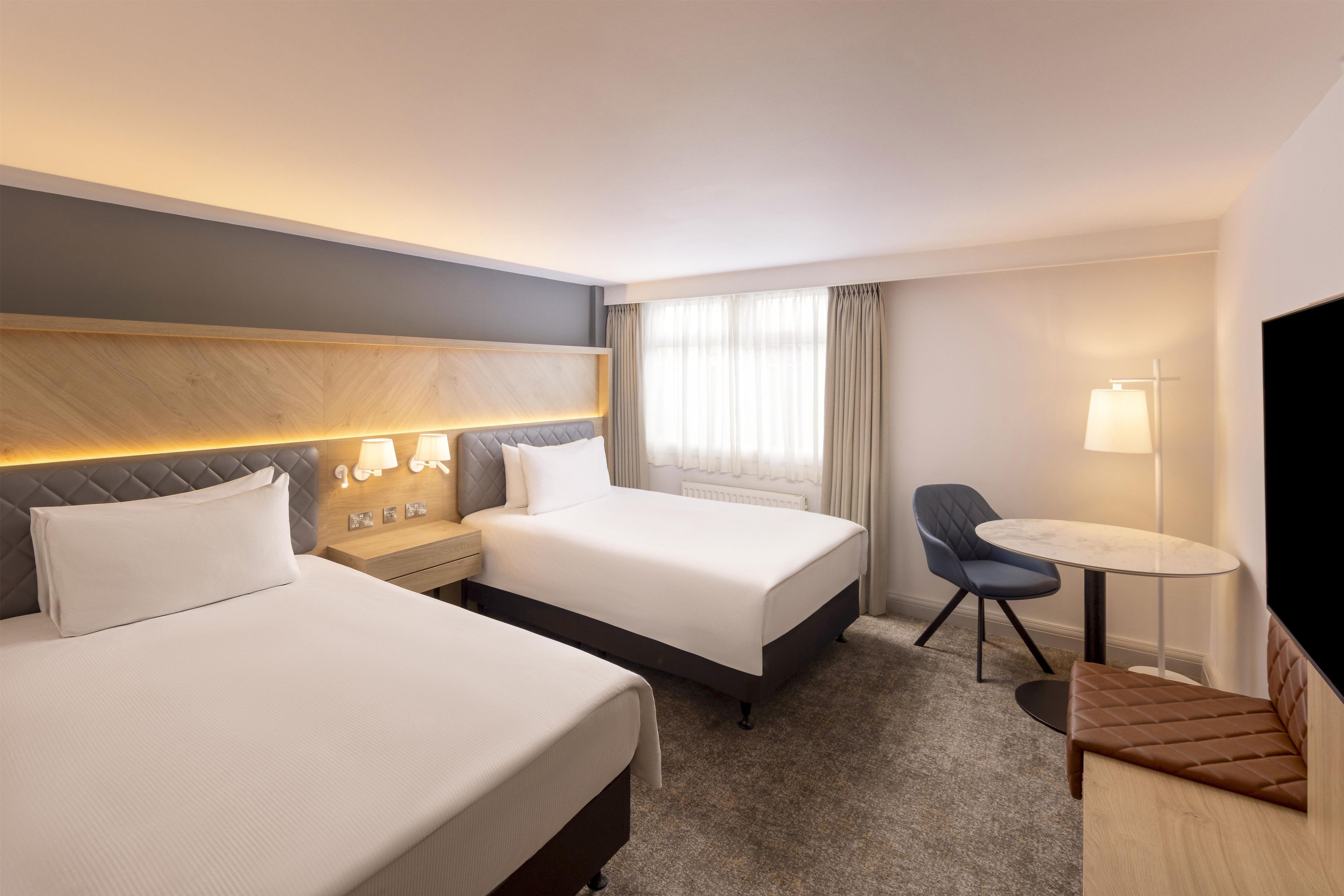 Habitación de hotel con dos camas, un escritorio, una silla y un televisor.