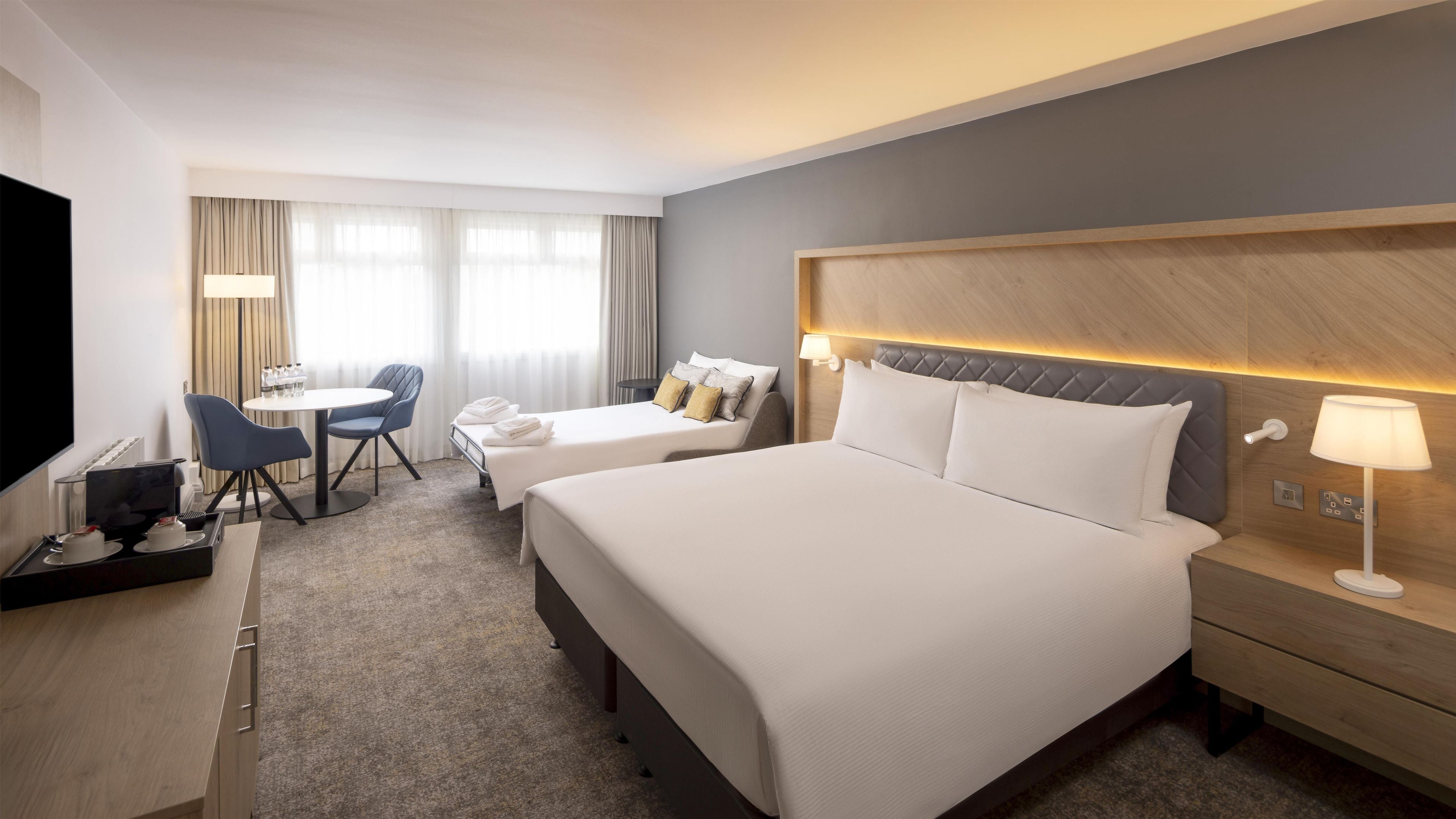 A hotel room with two beds, a desk with a coffee maker, a chair, and a TV.