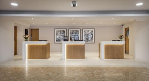 A hotel reception area with three wooden reception desks, a marble floor, and framed artwork on the wall.