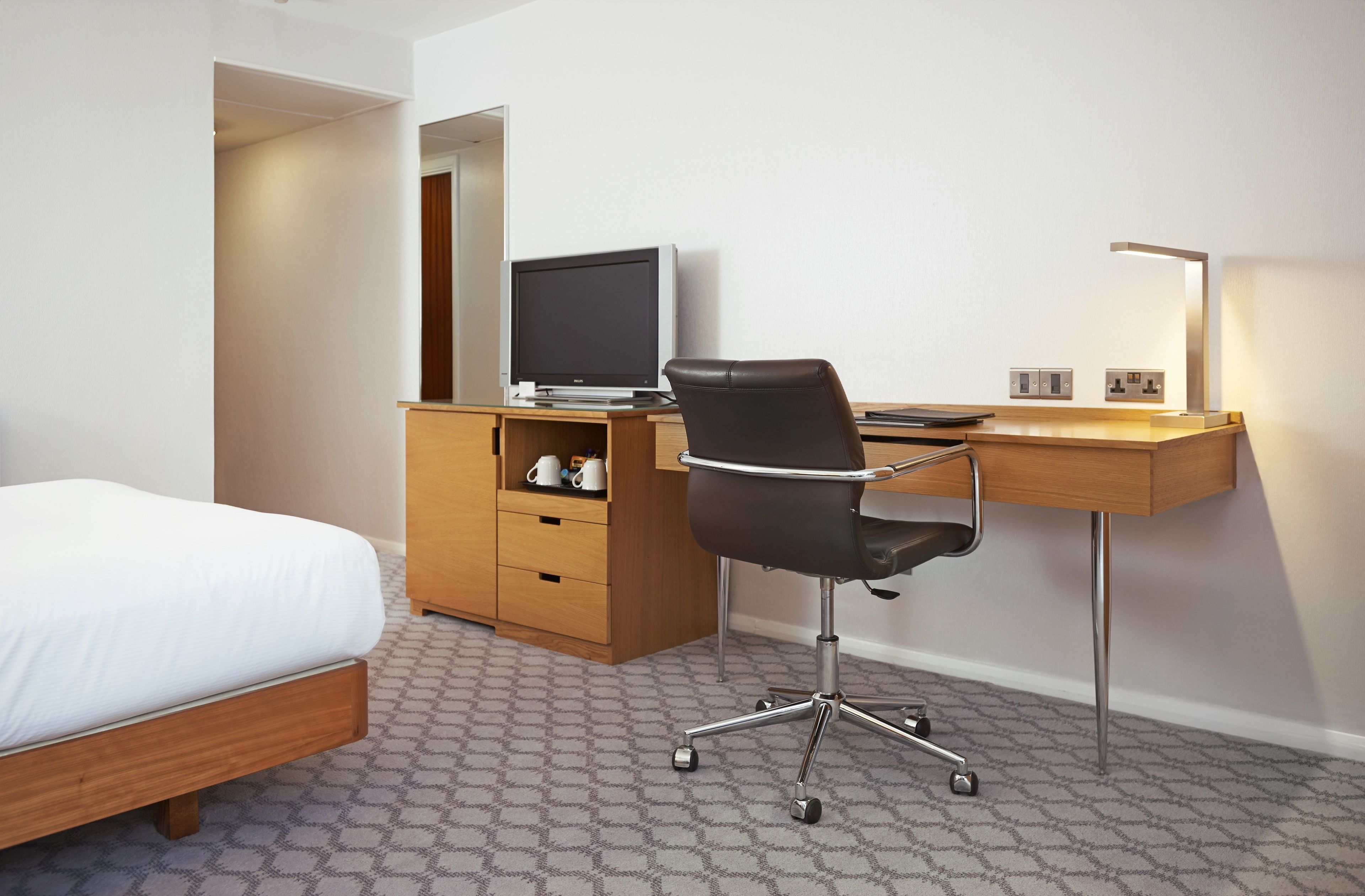 Una habitación de hotel con cama, escritorio con computadora, silla, lámpara y armario.