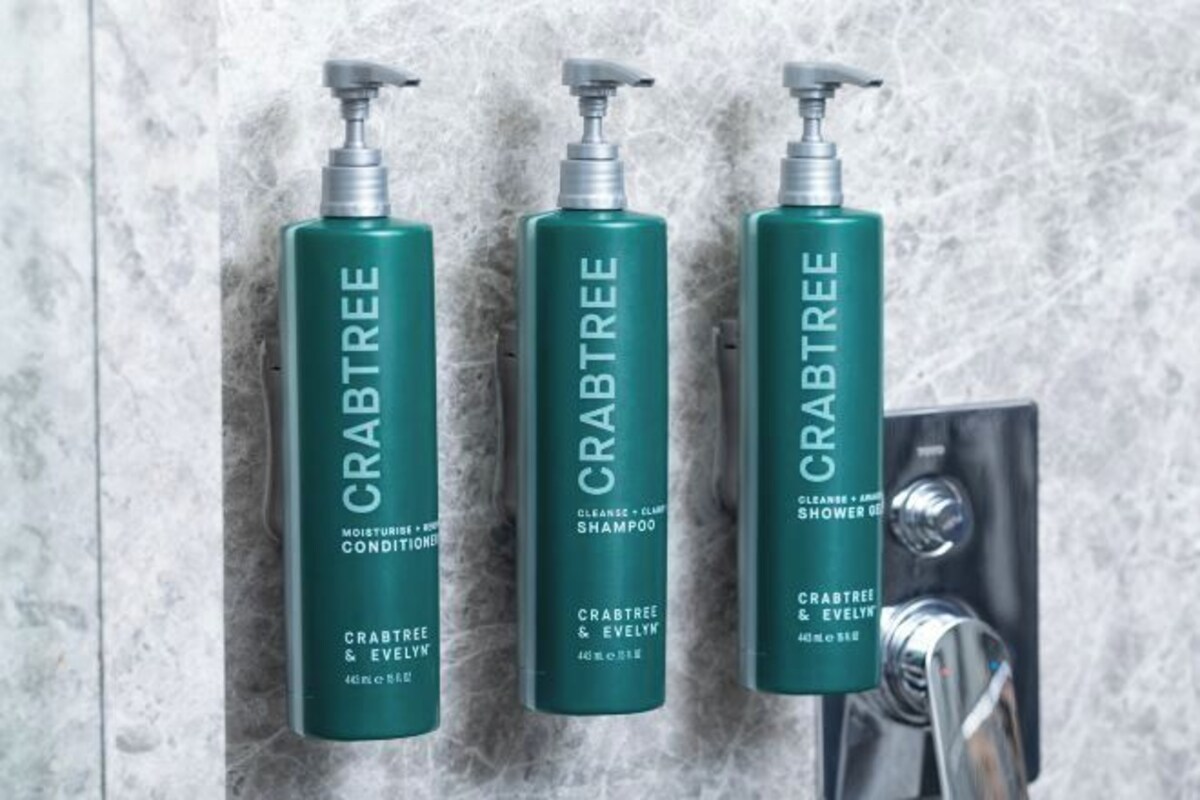 Three bottles of Crabtree & Evelyn shower gel and shampoo on a marble wall.