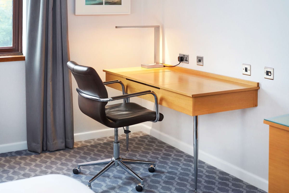 A modern office desk with a leather chair, a desk lamp, and a power outlet on the wall.