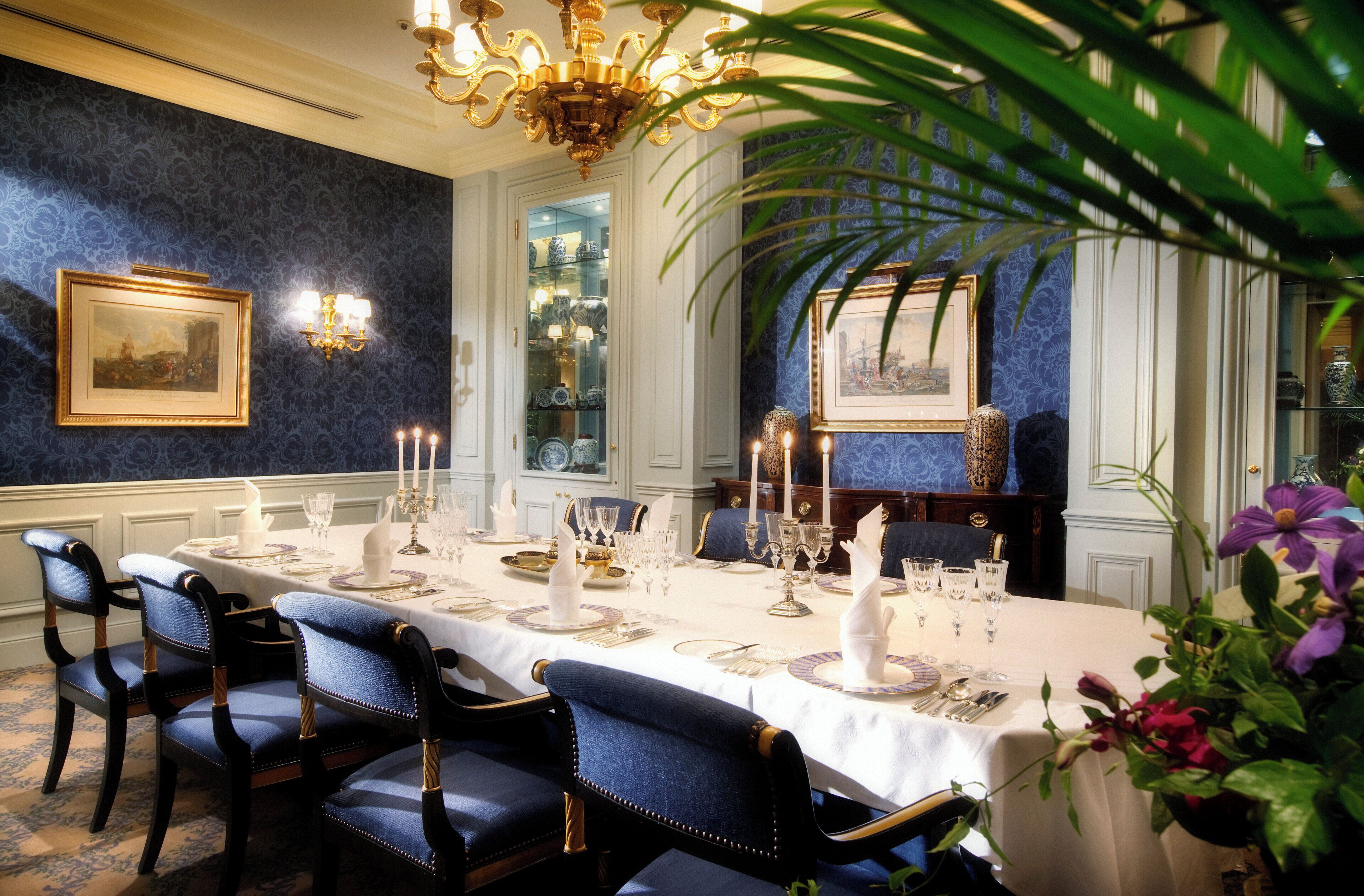 A formal dining room with a long table set for a meal, elegant chairs, and a chandelier.