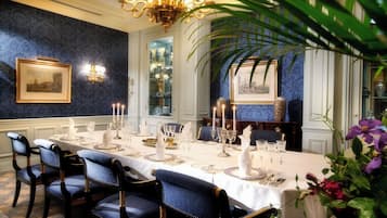 A formal dining room with a long table set for a meal, elegant chairs, and a chandelier.