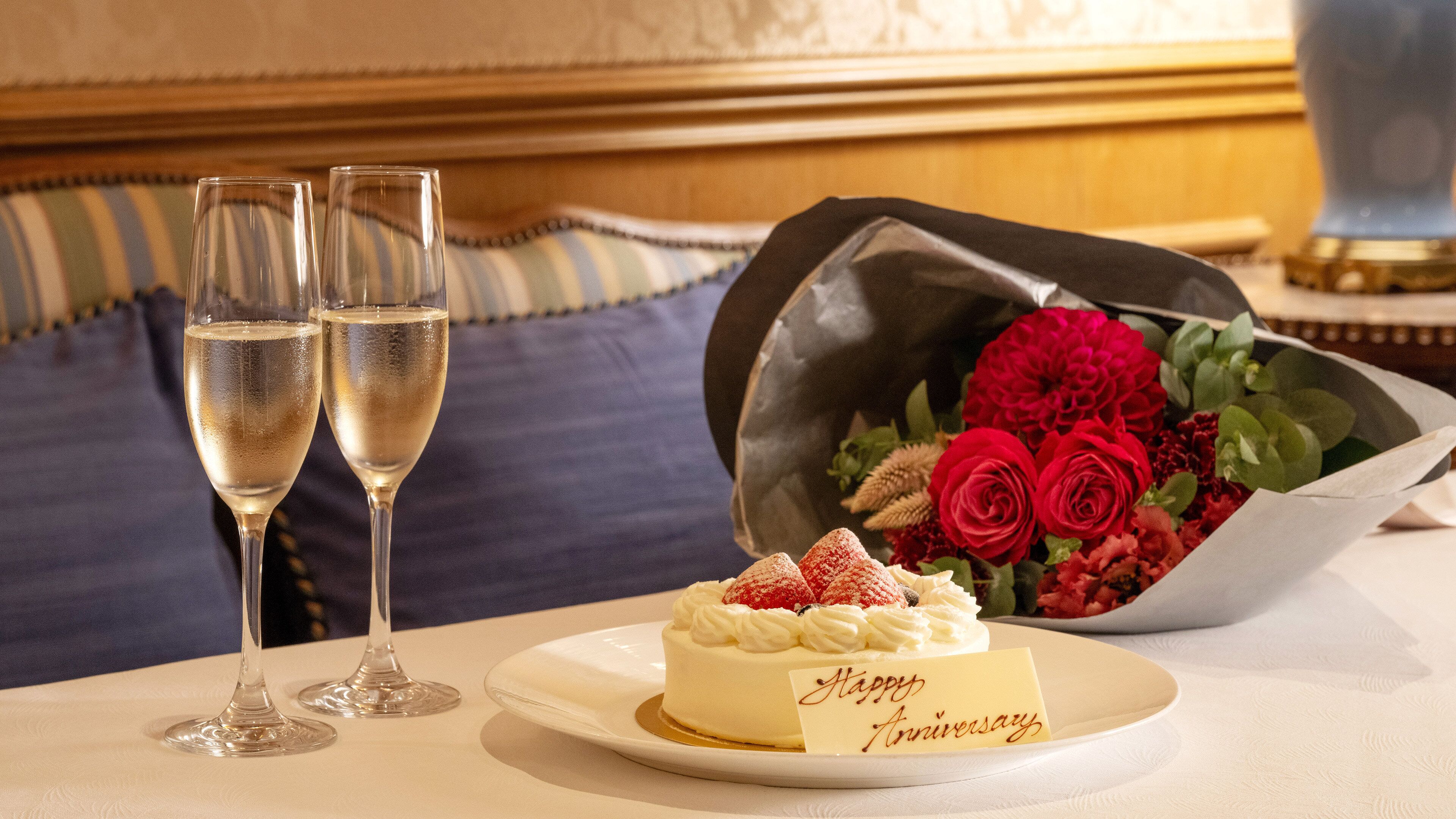 A dining table with a dessert plate, two champagne flutes, and a bouquet of red roses.