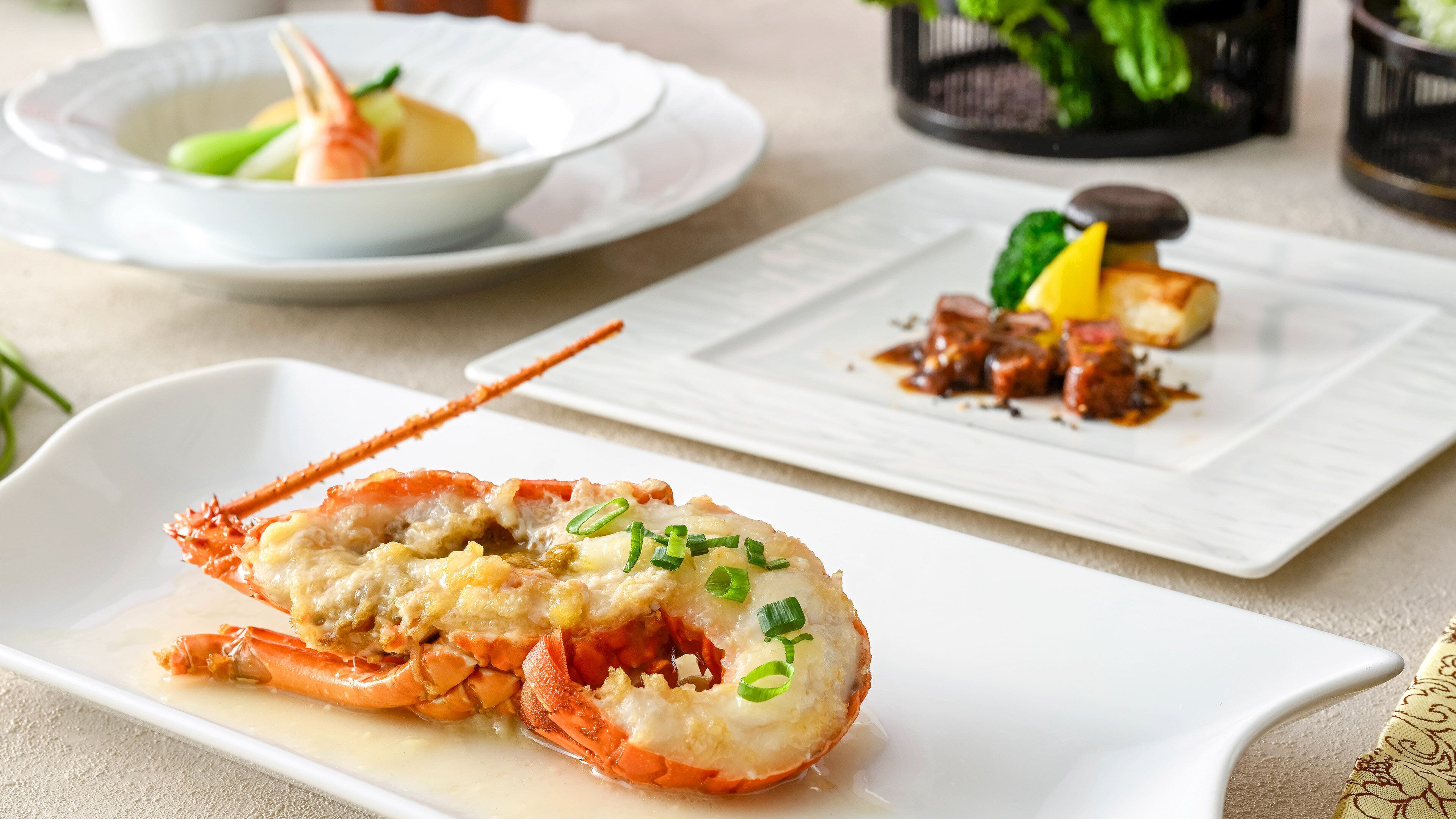 A lobster dish on a white plate with a side of vegetables and a small bowl of sauce.