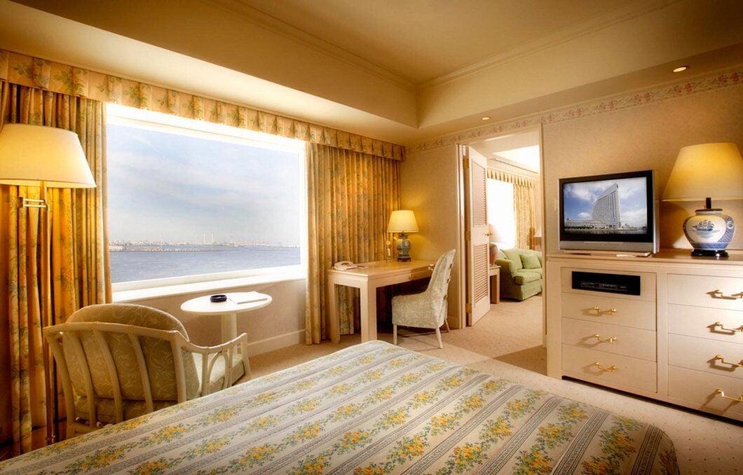A hotel room with a large bed, a desk, a chair, a television, and a view of the cityscape.