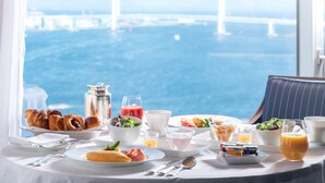Una mesa de desayuno con croissants, un frutero, un vaso de jugo y vistas de un puente sobre el agua.
