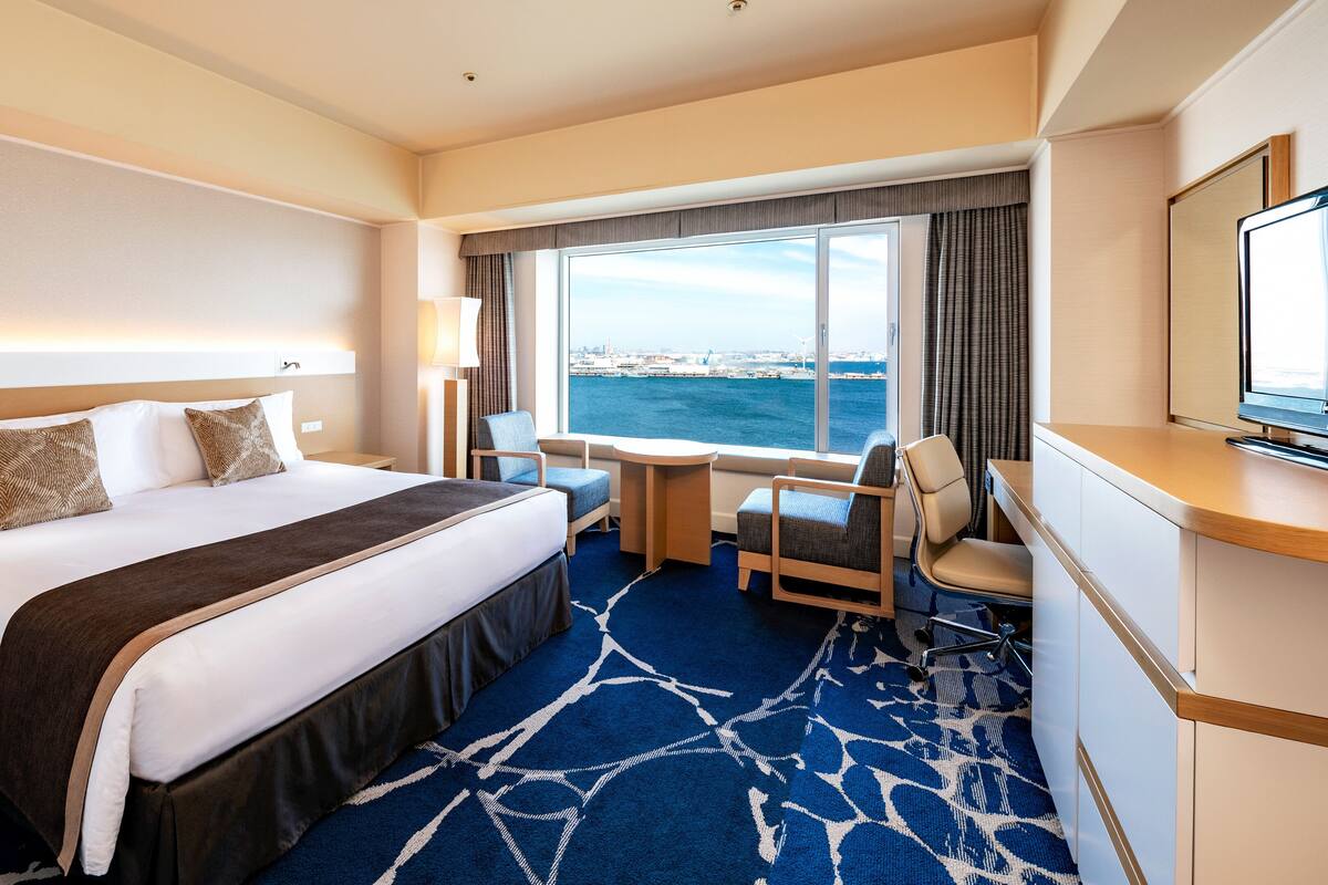 A hotel room with a large bed, a desk, a chair, and a view of the sea.