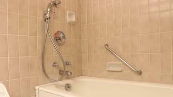 A bathroom with a bathtub, a handheld showerhead, a grab bar, and a control panel.