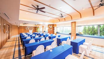 A conference room with rows of tables, ceiling fans, and a view of the outdoors.