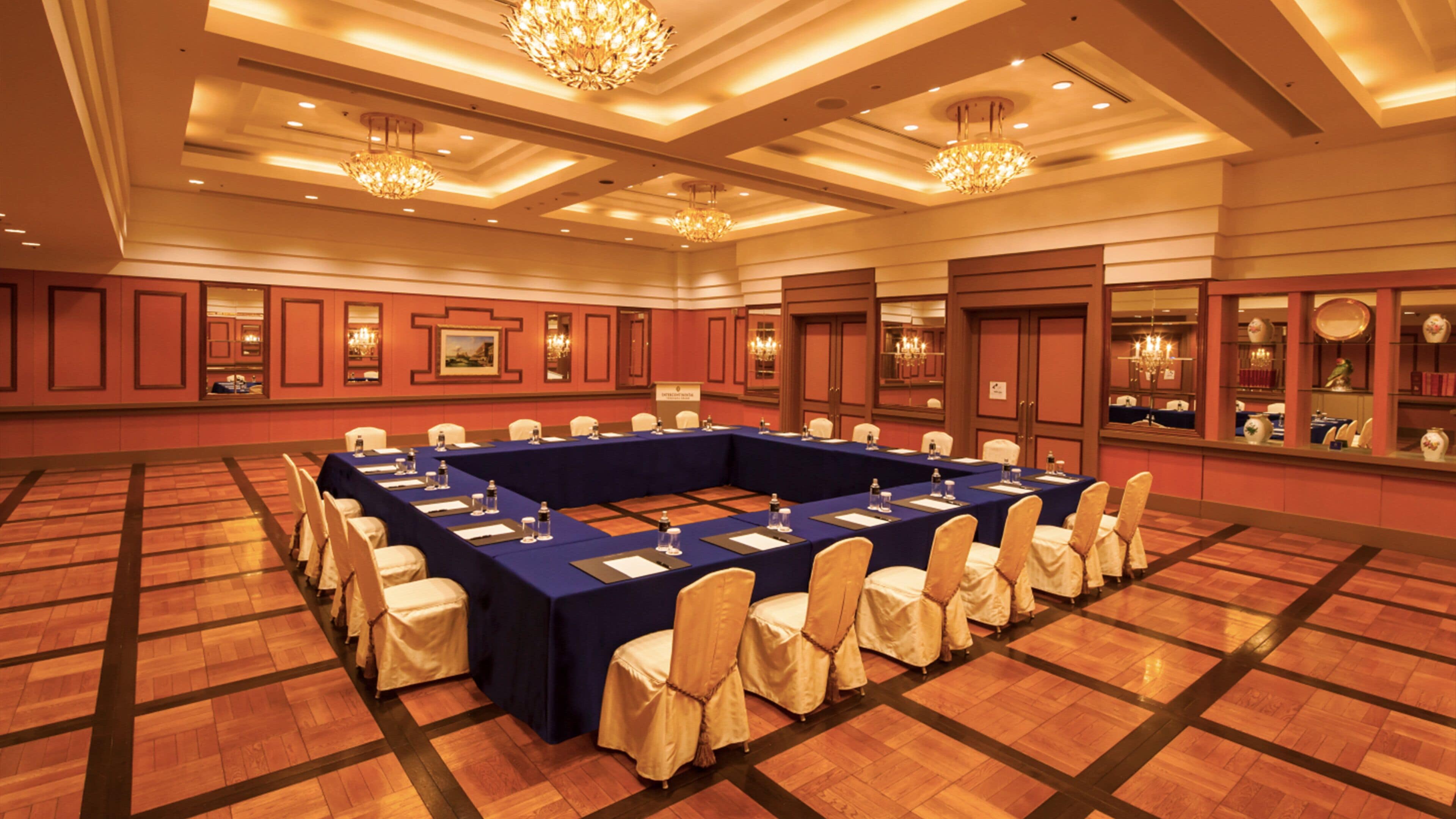 Un salón de conferencias con una larga mesa, sillas y candelabros.