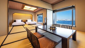 Habitación de hotel con suelo de esteras de tatami tradicionales, dos camas, una mesa de comedor y un amplio ventanal con vistas al mar.