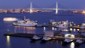 Un puerto con un puente grande al fondo, varias embarcaciones amarradas y un edificio con un espacio abierto amplio.