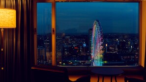 A view from a window with a cityscape at night, featuring illuminated buildings and a prominent tower with colorful lights.
