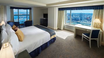A hotel room with a large bed, a desk, a chair, a TV, and a view of a cityscape.