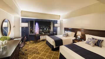 Habitación de hotel con dos camas, un escritorio, una silla y vista a un paisaje urbano nocturno.