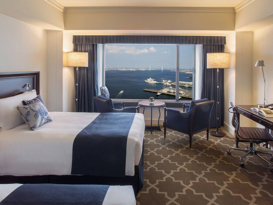 A hotel room with a large bed, a desk, a chair, and a view of the water.