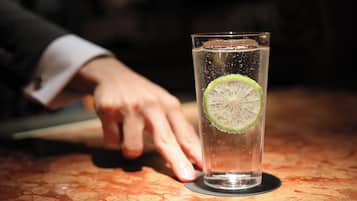Una copa de vidrio transparente con una rodaja de lima y burbujas, sobre una mesa donde una mano se extiende hacia ella.