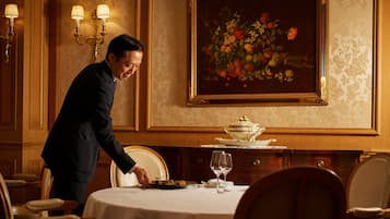 A man serving food at a table in a room with a floral painting and a gold-framed mirror.