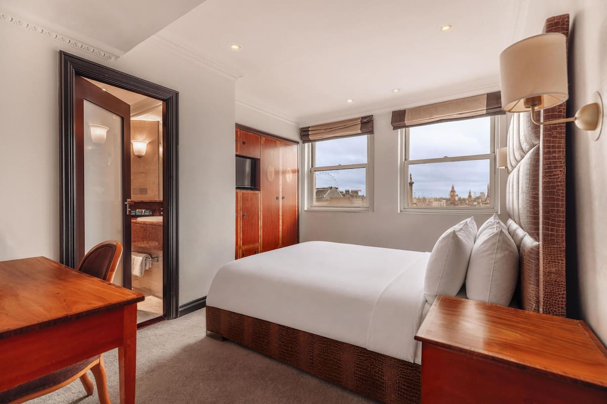A hotel room with a bed, a desk, a chair, a wardrobe, and a window with a city view.