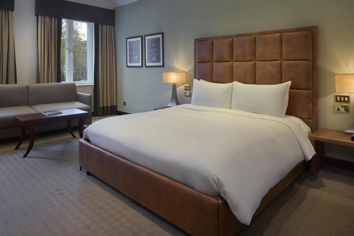 A hotel room with a large bed, a sofa, a nightstand, and a lamp.