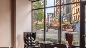 Un intérieur moderne avec une grande fenêtre, des fauteuils en cuir, une petite table ronde et une vue sur une rue animée.