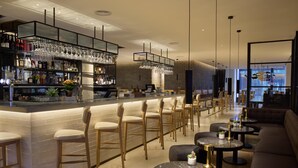 Un espace bar moderne avec un long comptoir, des tabourets de bar et des tables rondes.