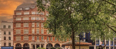 A historic building with arched windows and a brick facade, surrounded by greenery and a statue.