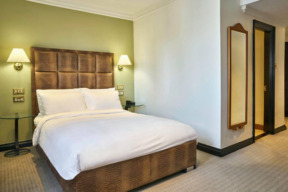 A hotel room with a large bed, two bedside lamps, a glass side table, and a mirror on the wall.