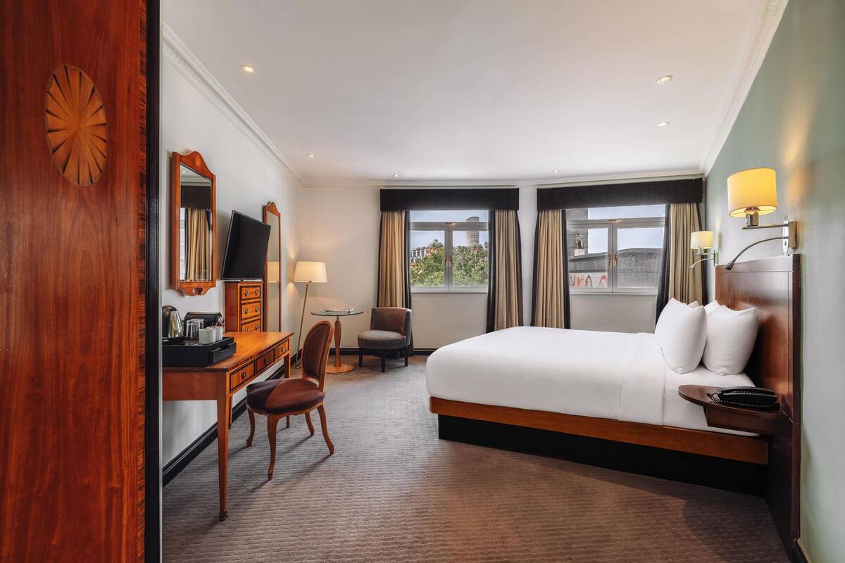 A hotel room with a large bed, a desk with a chair, a small table, and a TV.