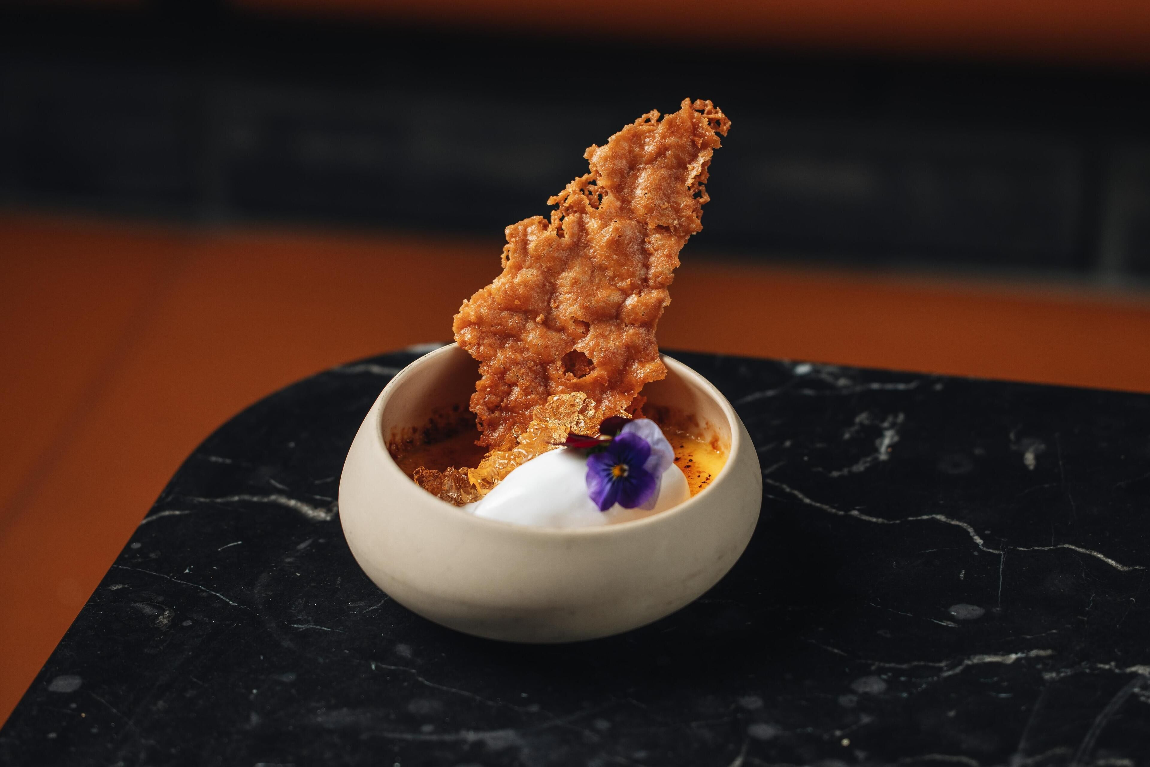 A dessert in a small bowl on a black marble surface.