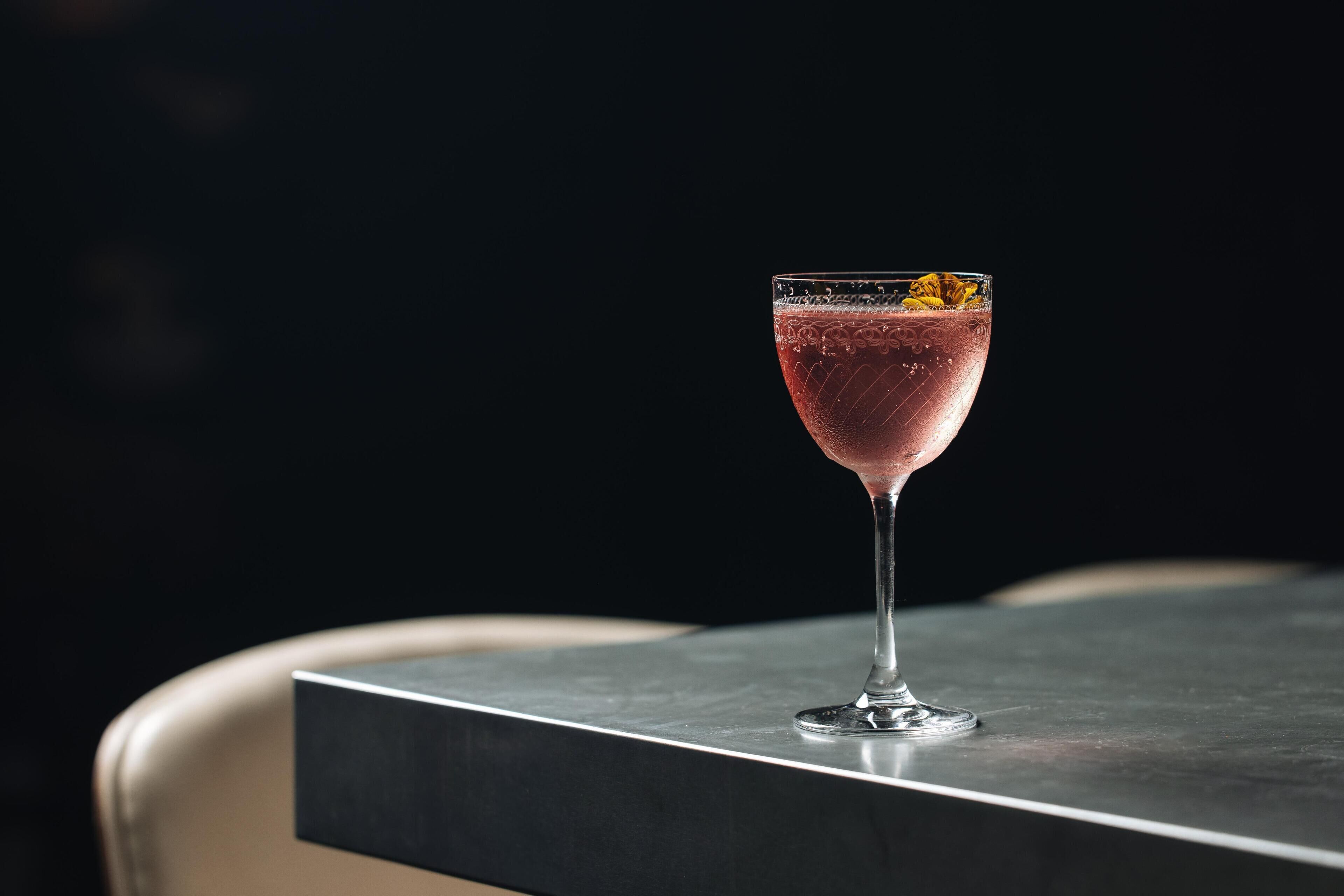A glass of pink drink on a table with a dark background.