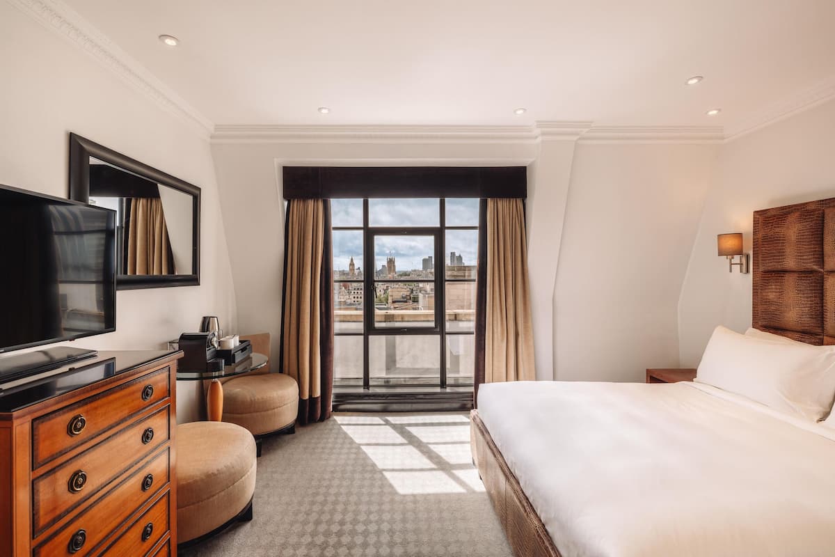 A hotel room with a bed, a television, a dresser, a chair, a desk, and a window with a city view.