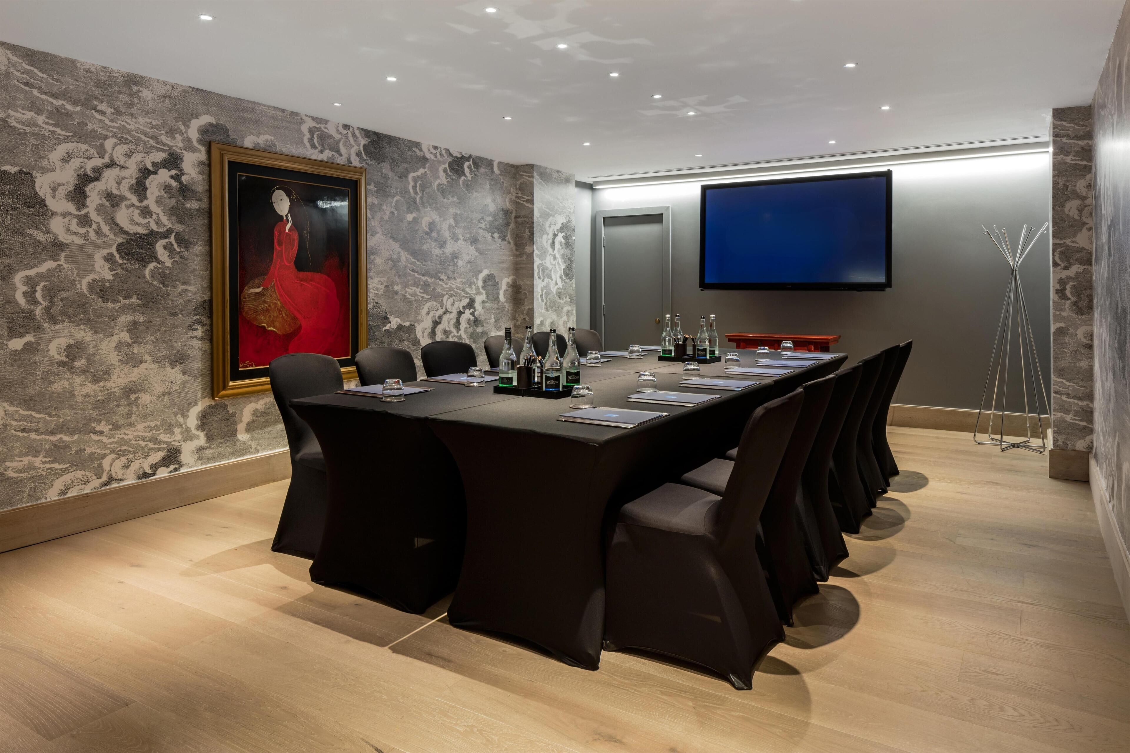 A conference room with a long table, chairs, a painting, a TV screen, and a floor lamp.