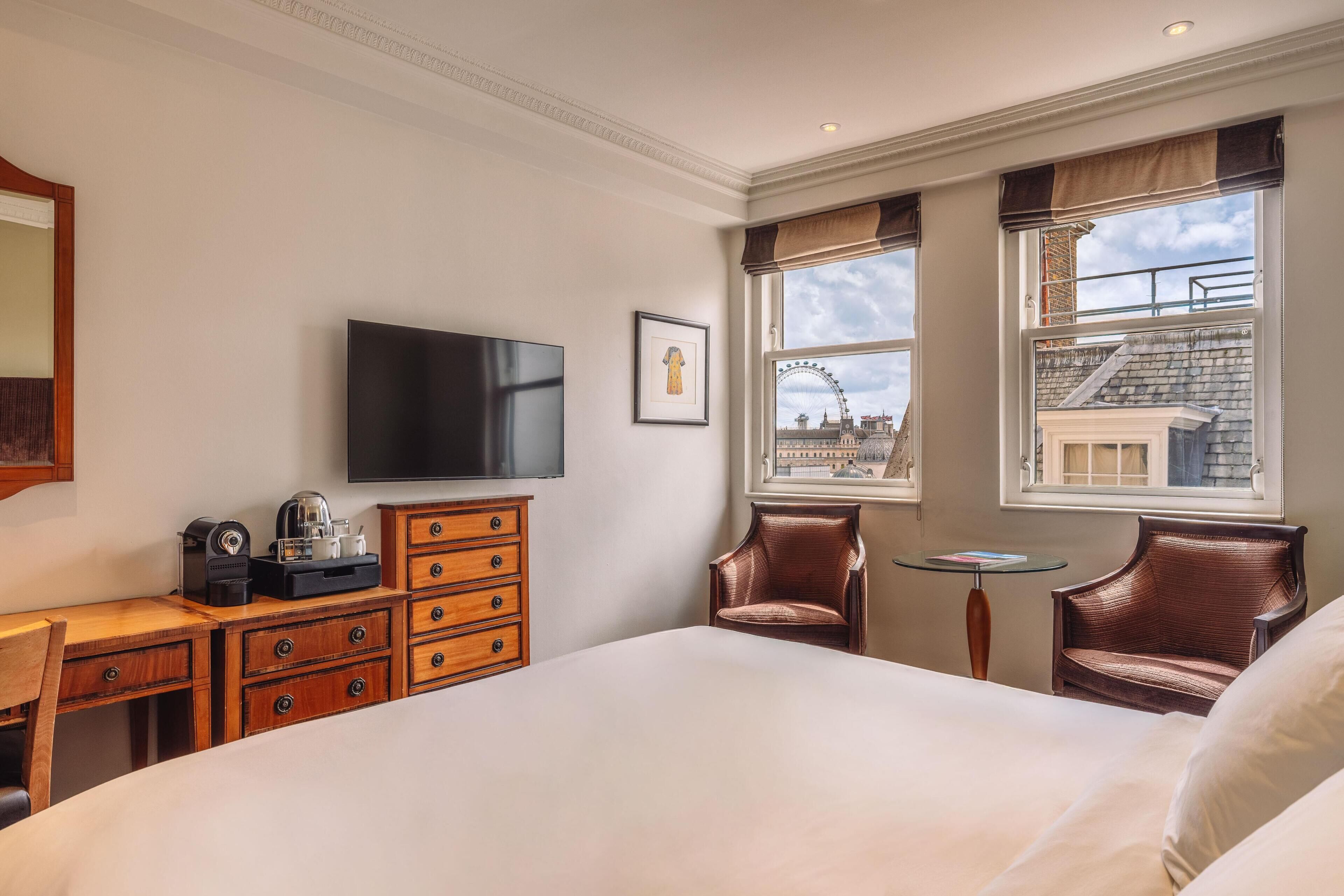 A hotel room with a bed, a desk with drawers, a television, two chairs, a small table, and a window with a view of a Ferris wheel.