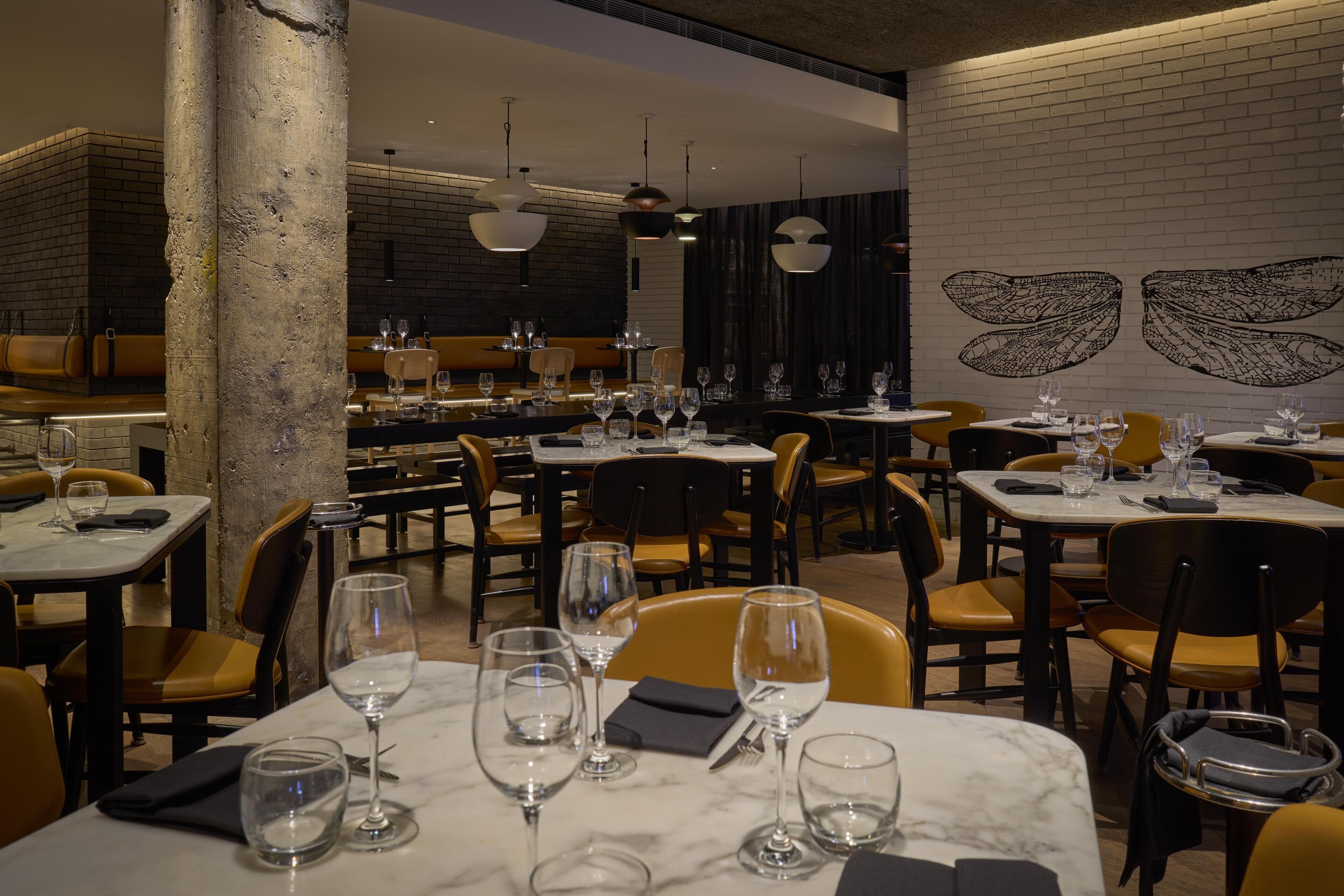 A restaurant with marble tables, yellow chairs, and a brick wall with a winged design.
