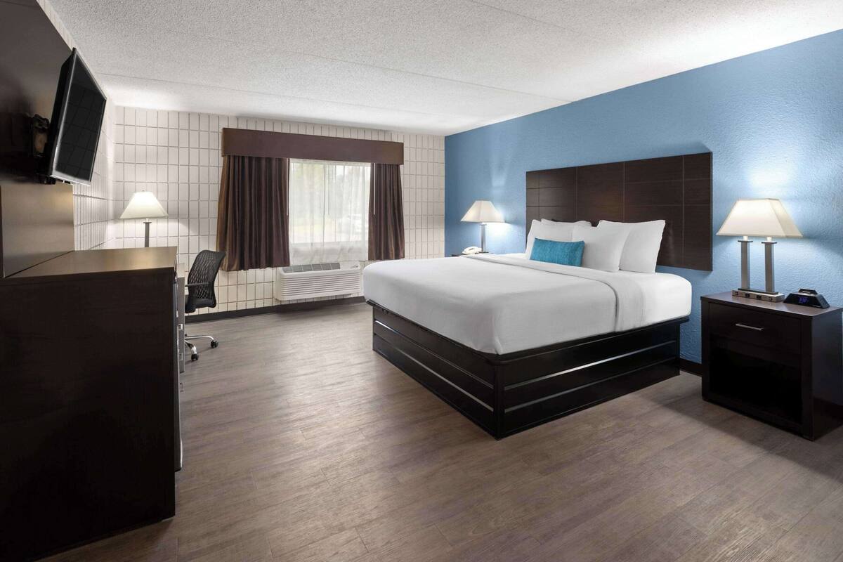 Een hotelkamer met een groot bed, twee nachtkastjes met lampen, een bureau, een stoel en een aan de muur bevestigde televisie.